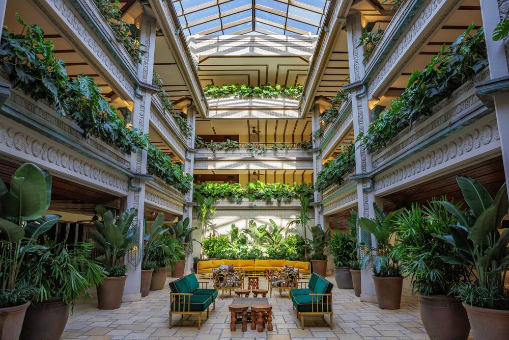 Elegant indoor courtyard with glass ceiling, classical columns and abundant tropical greenery.