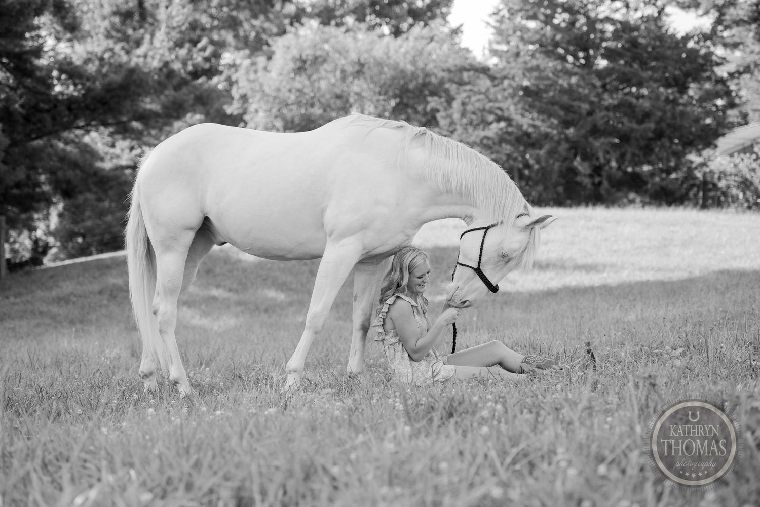 A white horse grazing in a black and white pastoral scene with trees.