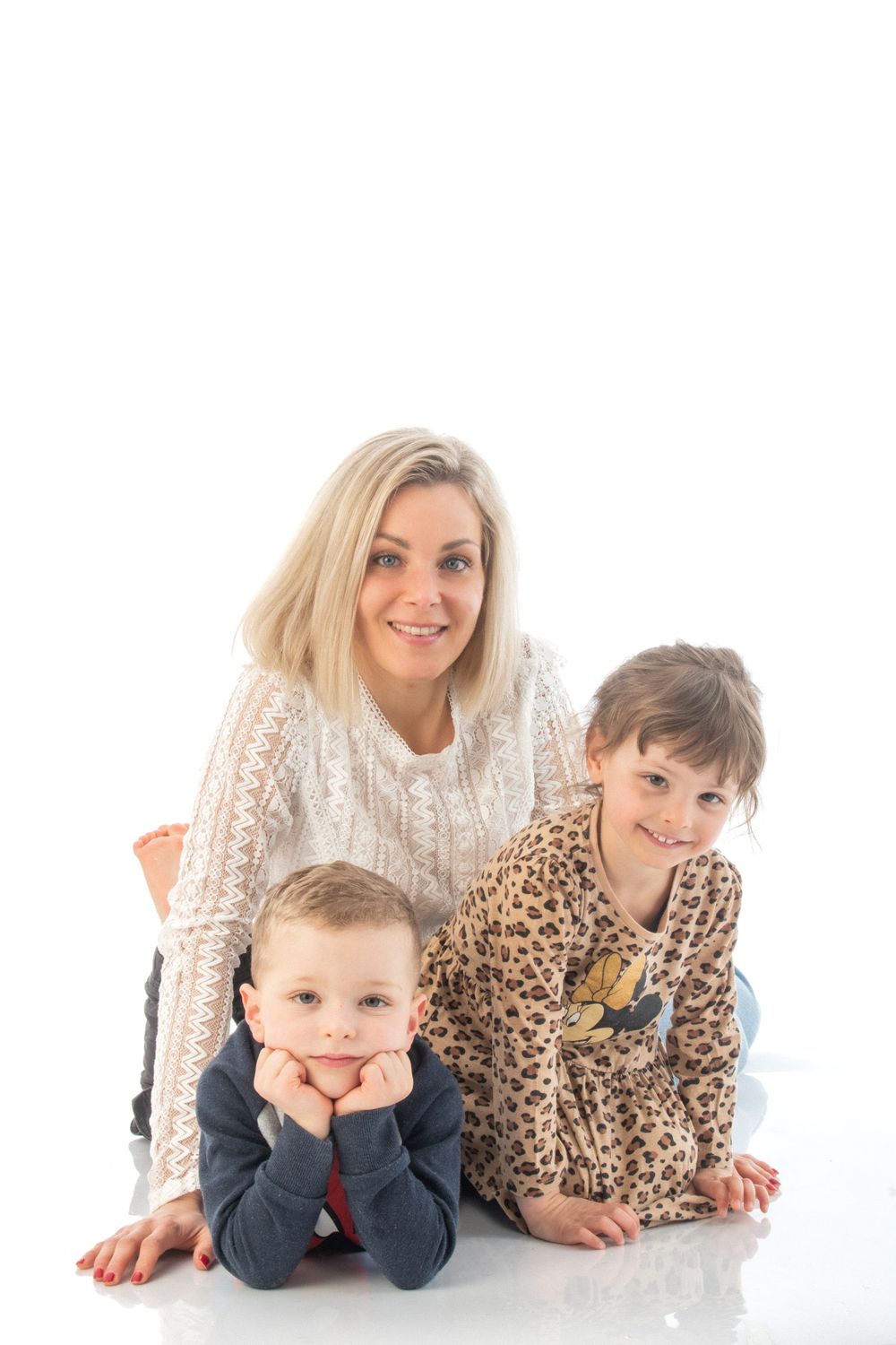 A casual studio portrait showing a parent and two children lying on white floor.