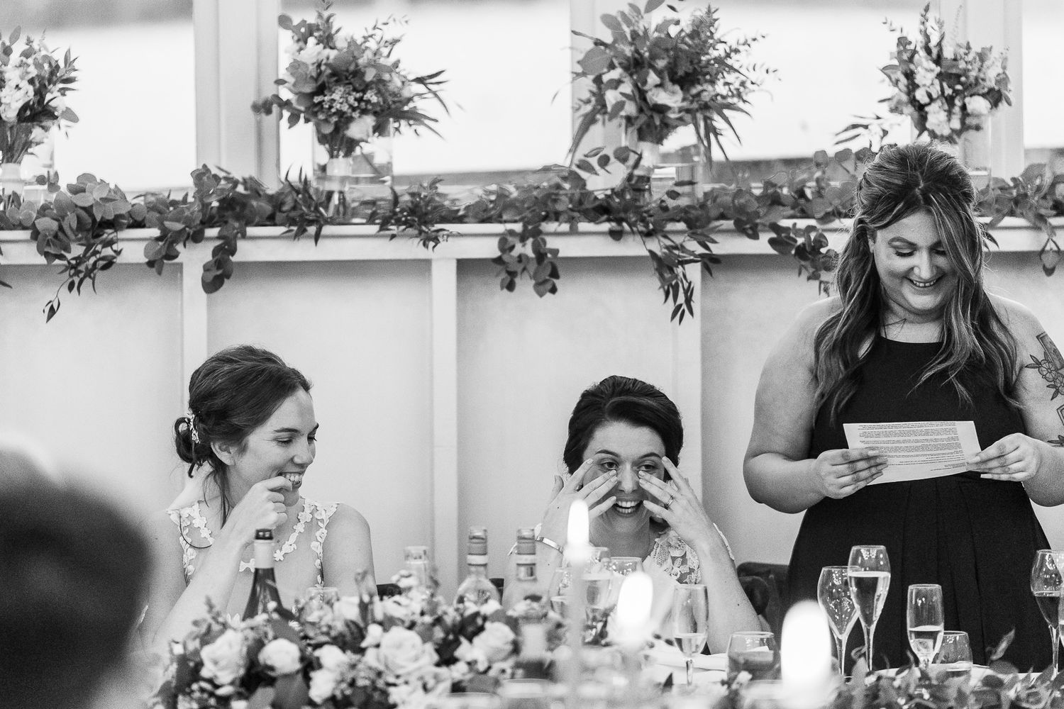 Wedding guests react emotionally during speeches at an elegant reception decorated with floral garlands.