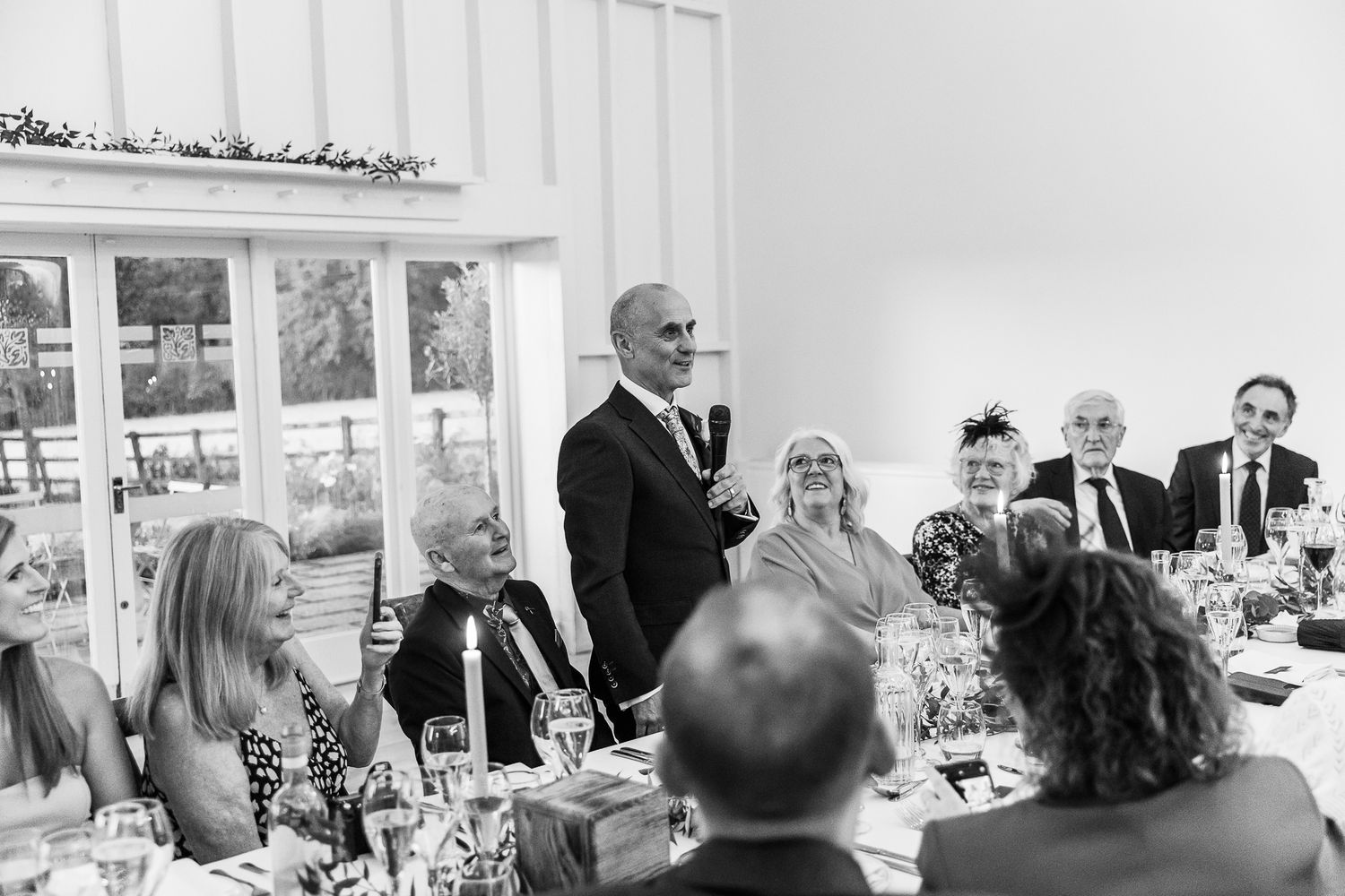A speaker delivers a heartfelt toast during a wedding reception while guests listen attentively.