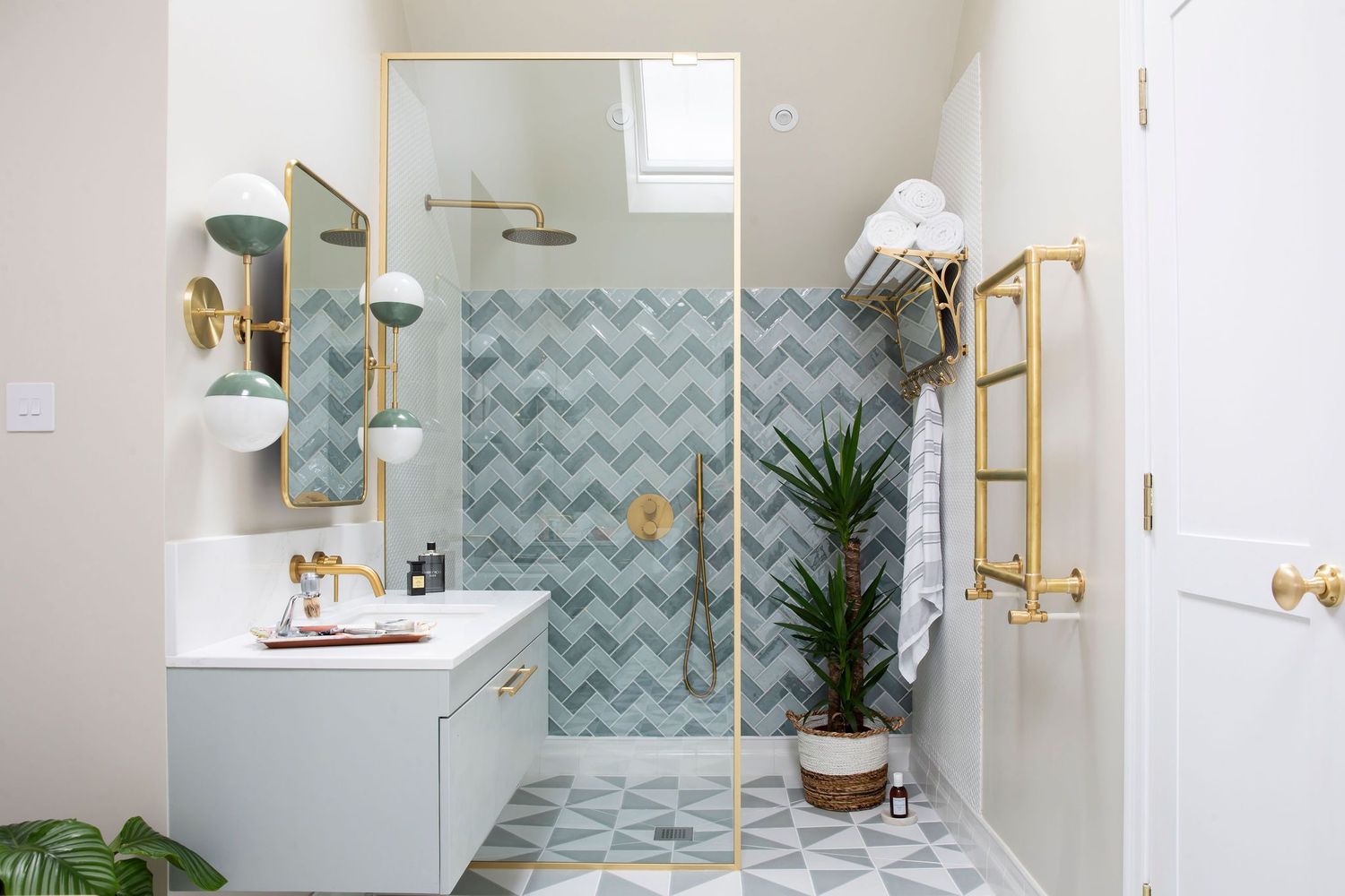 Modern bathroom with chevron tile pattern, gold fixtures, and glass shower enclosure featuring blue-grey and white color scheme.