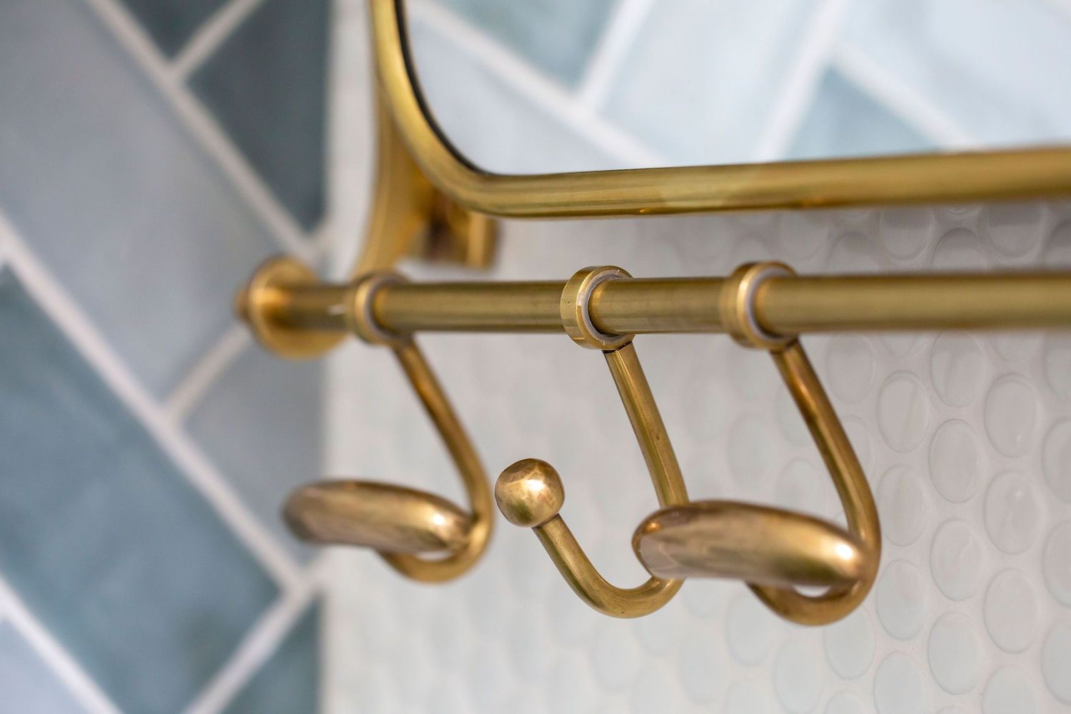Close-up detail of brass towel hooks mounted on blue tile bathroom wall.