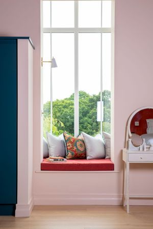 Pink-walled room with built-in window seat, navy cabinet, and vanity mirror.