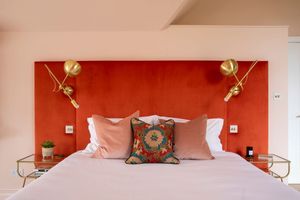 Modern bedroom with coral accent wall, gold sconces, and pink pillows on a white bed.