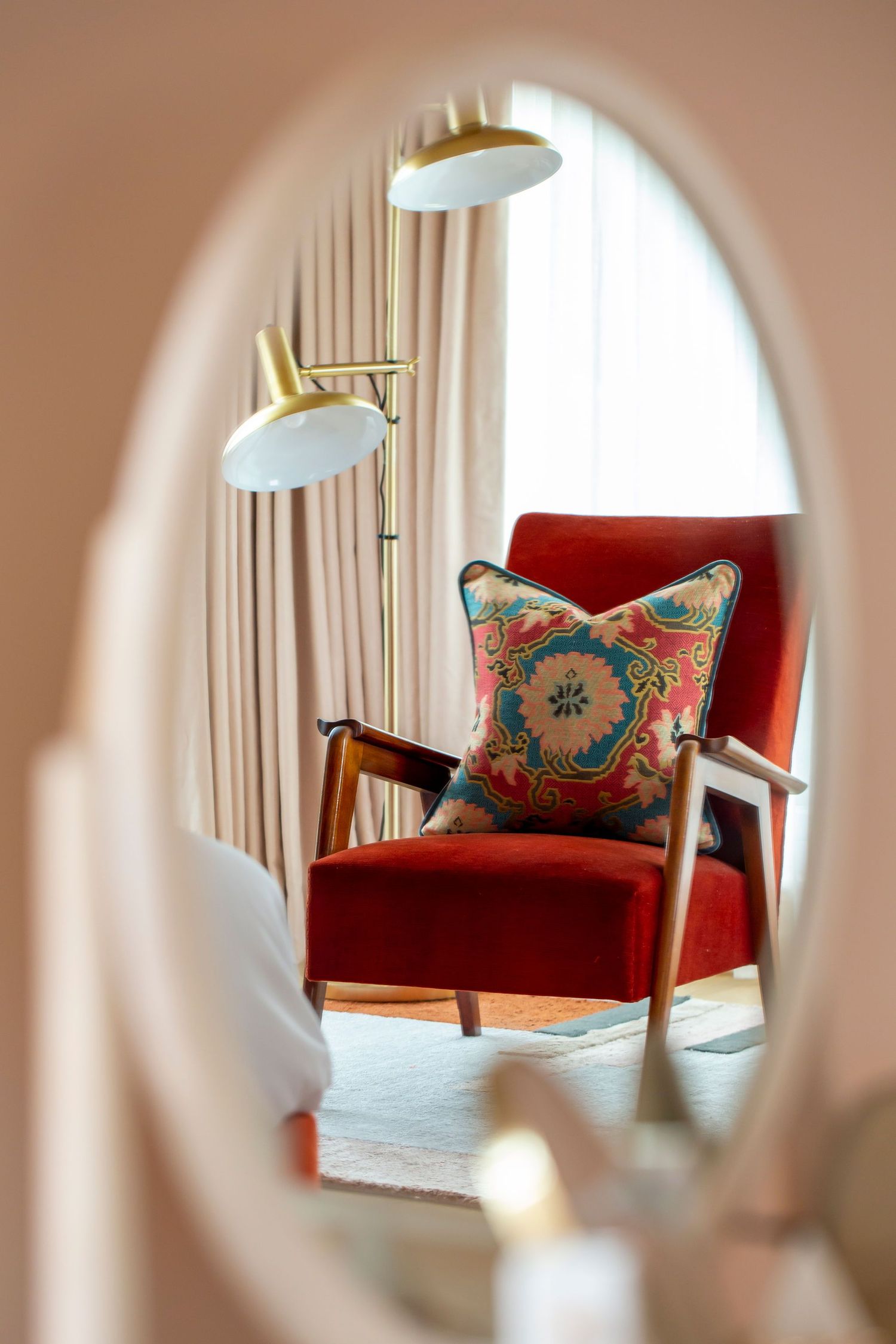 Red velvet armchair with decorative pillow viewed through oval mirror reflection.