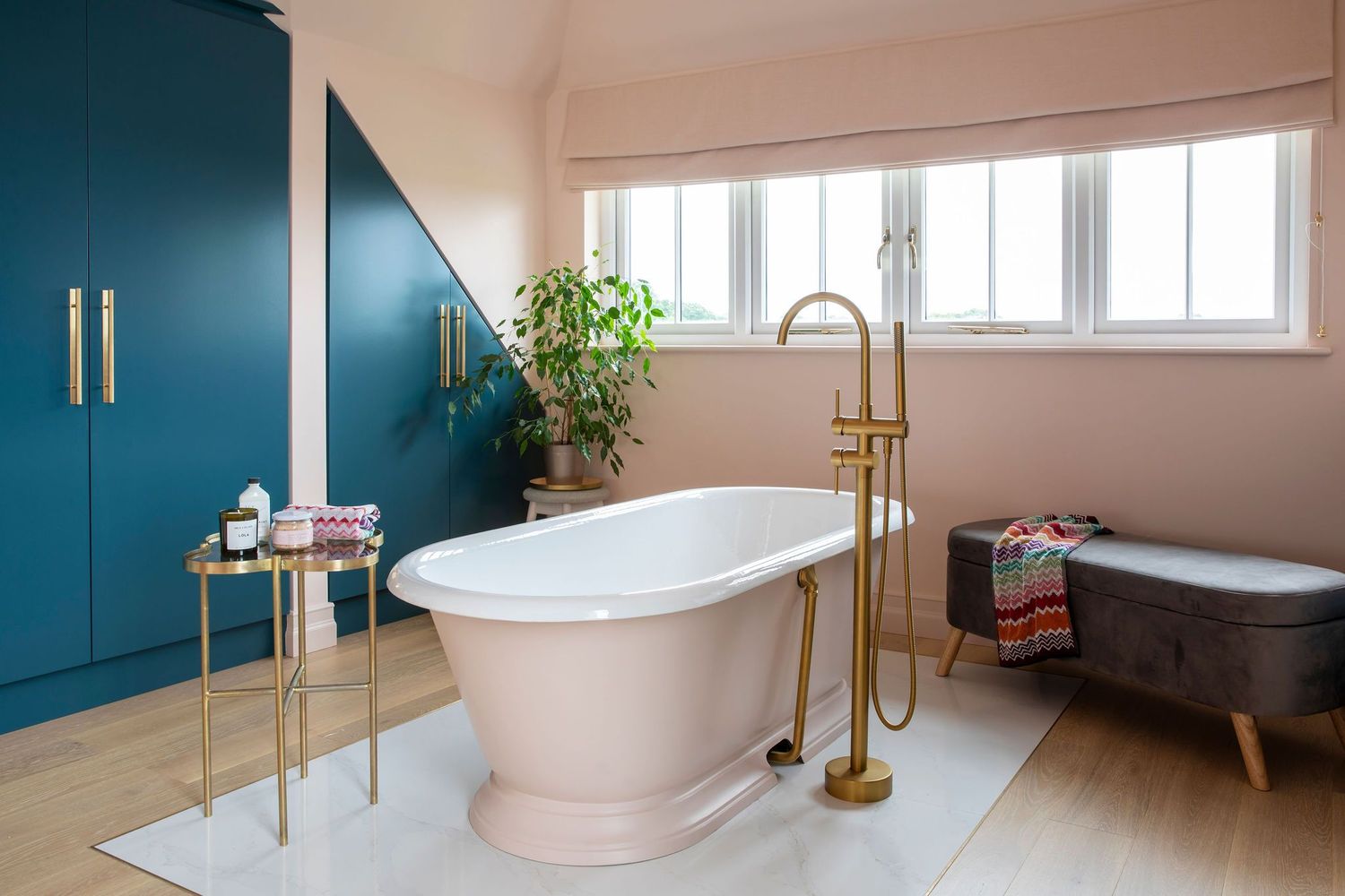 Luxurious bathroom with freestanding tub, brass fixtures, and teal built-in storage cabinets.