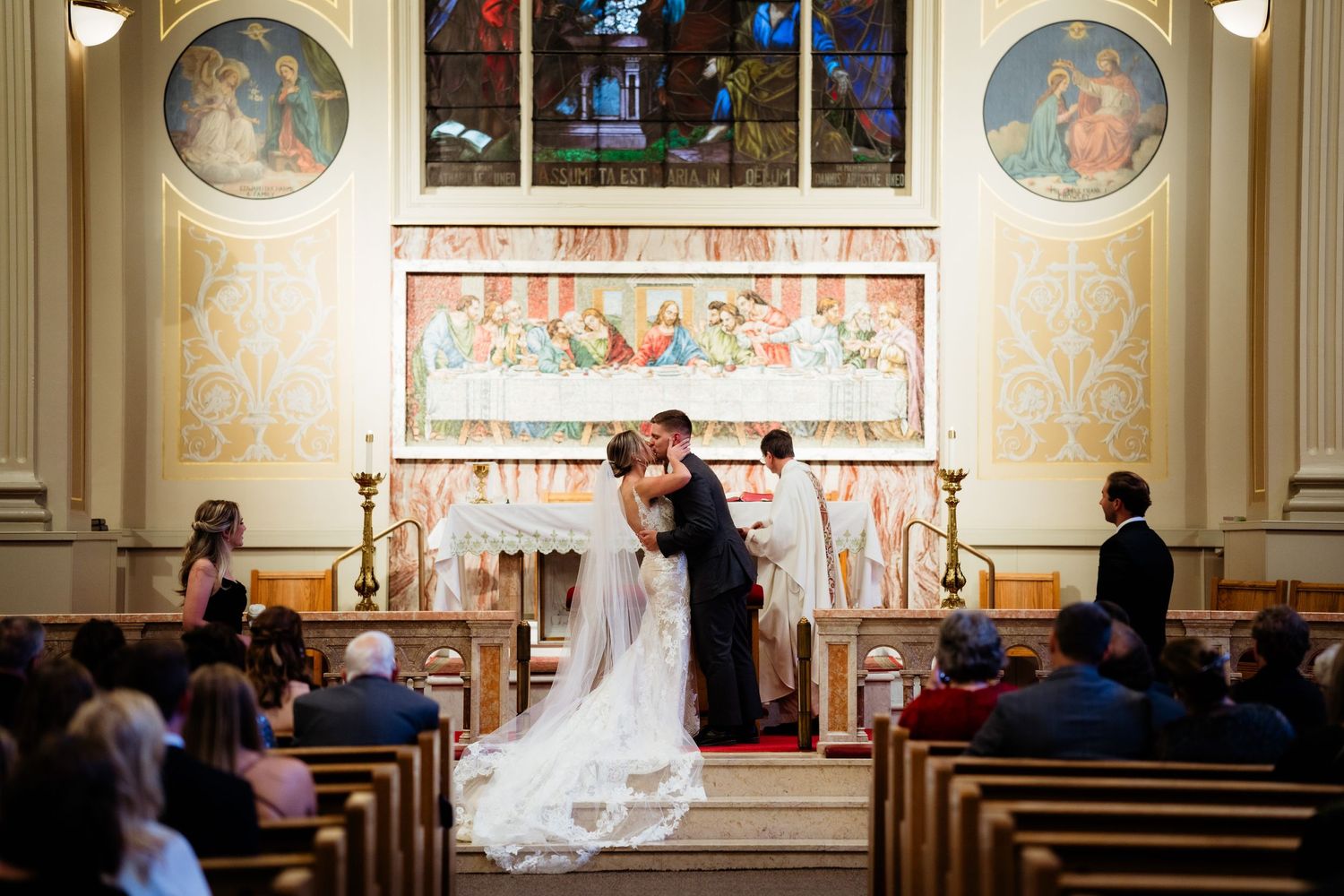 Wedding ceremony in progress at an ornate church with painted murals and stained glass windows.