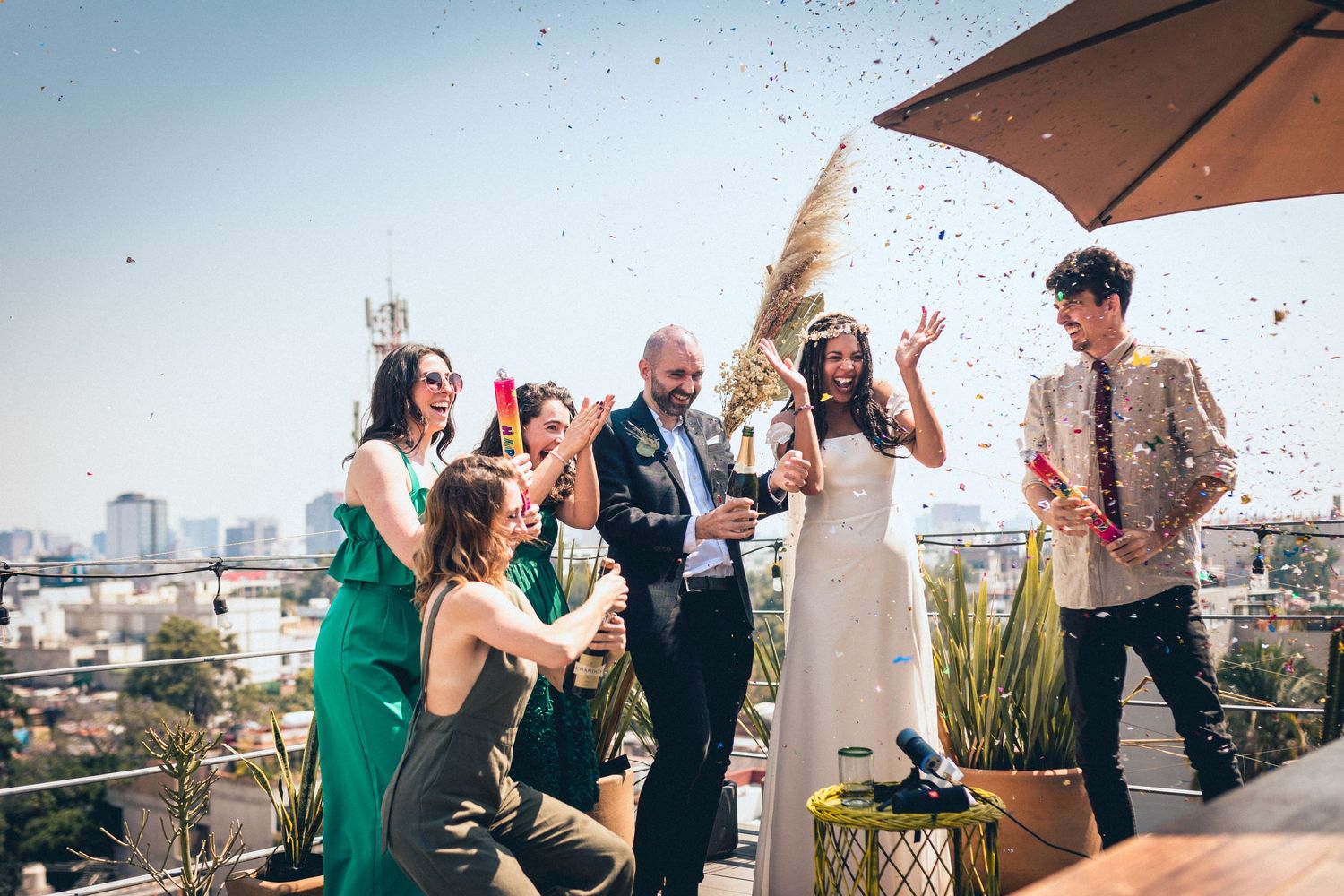 Wedding party celebrating with confetti and champagne on a rooftop terrace.