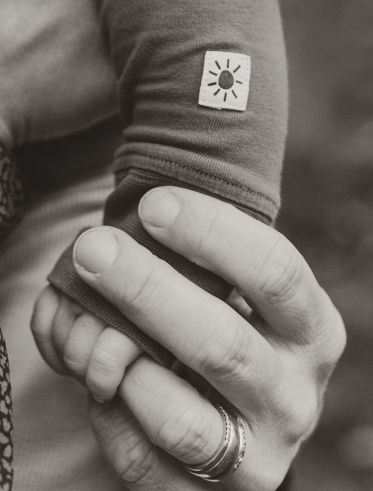 Close-up black and white photo of hands with a sun icon patch on clothing sleeve.
