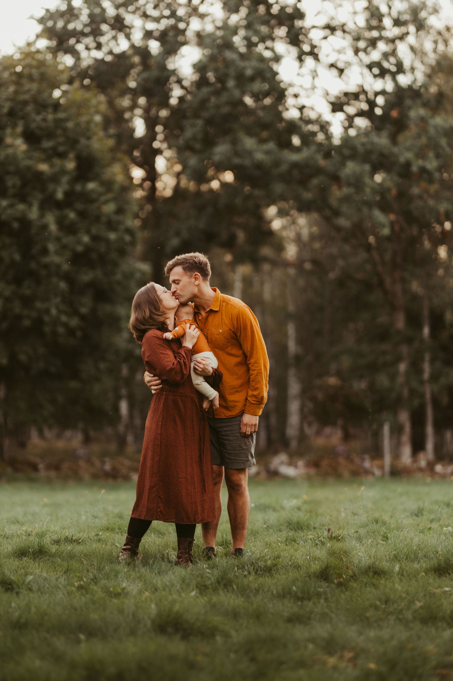 Family stands together in a grassy meadow at sunset wearing coordinating autumn colors.