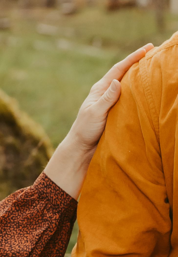 Close-up of hands touching an orange fabric shoulder in natural outdoor lighting.