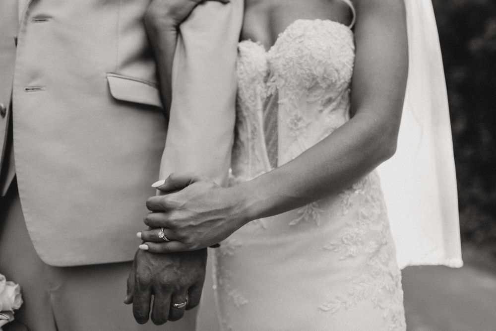 Black and white detail shot of wedding couple's hands and formal attire.