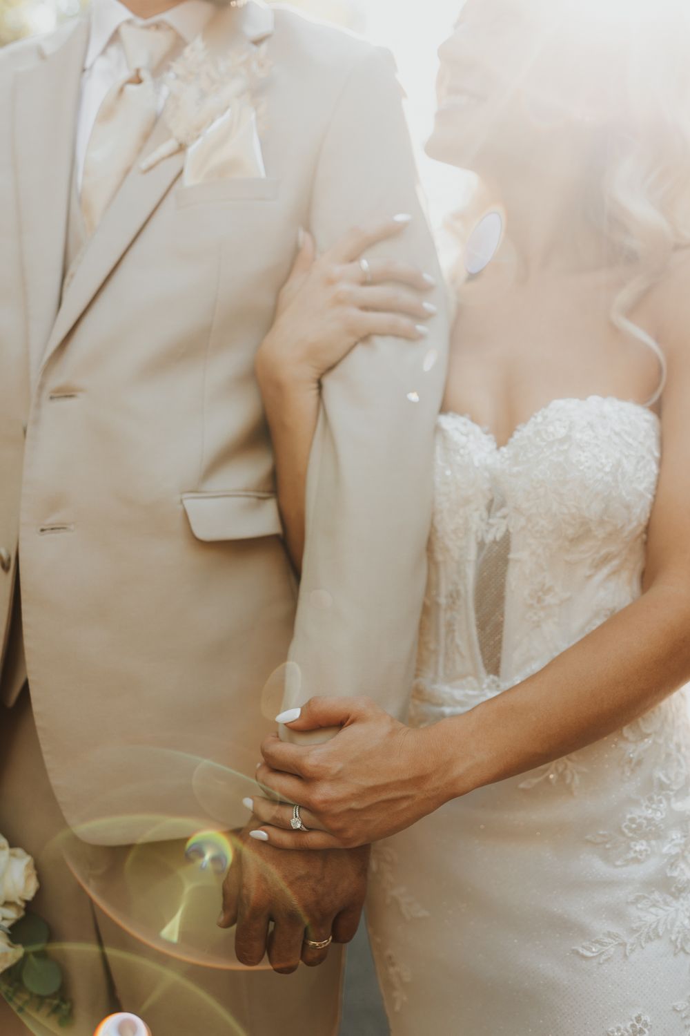Close-up wedding photo showing hands and formal attire in soft beige and white tones.