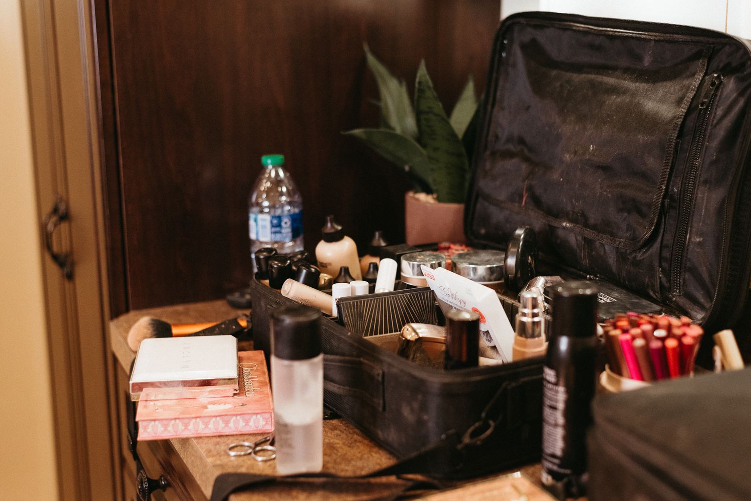 A messy vanity setup with makeup products, bottles, and beauty supplies scattered on a wooden surface.