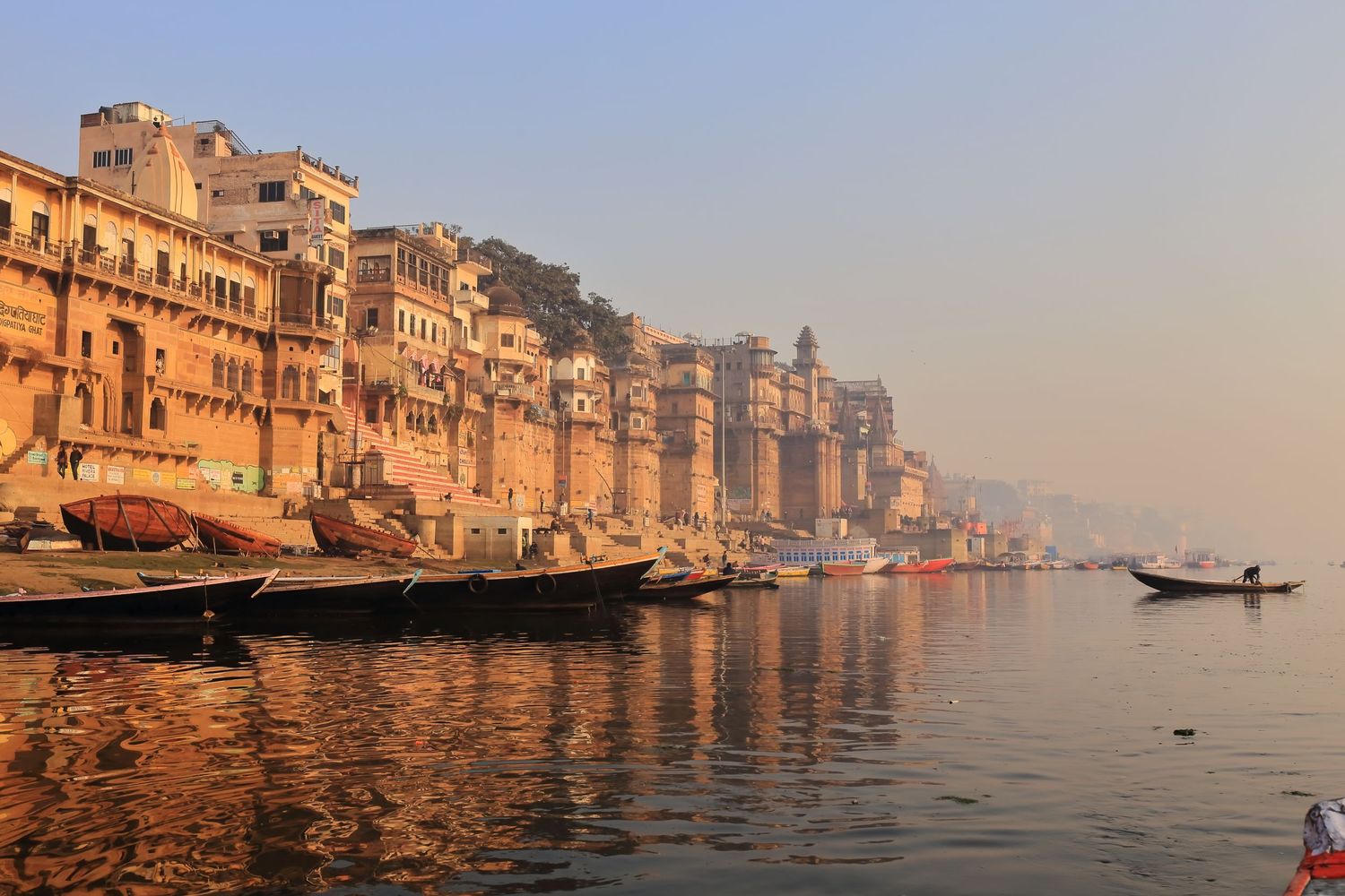 Historic buildings and boats line the sacred Ganges River waterfront in Varanasi at sunrise.