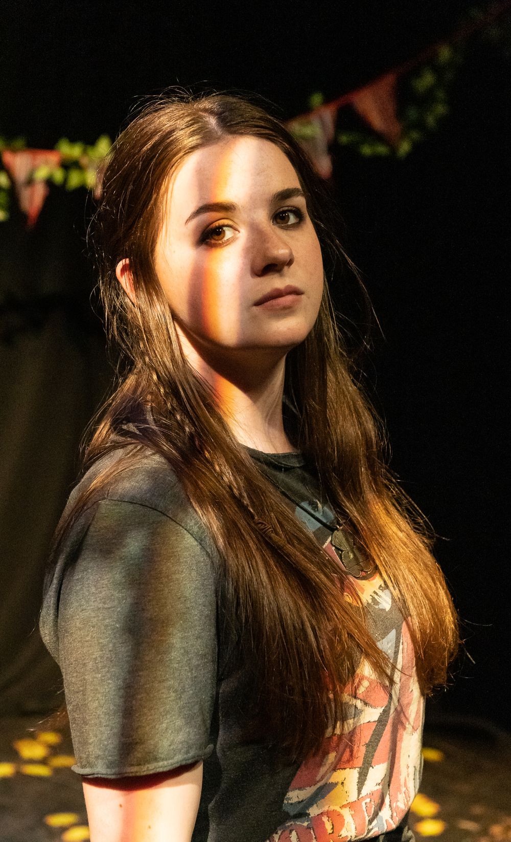 Portrait of young woman with long brown hair in band t-shirt under dramatic lighting.