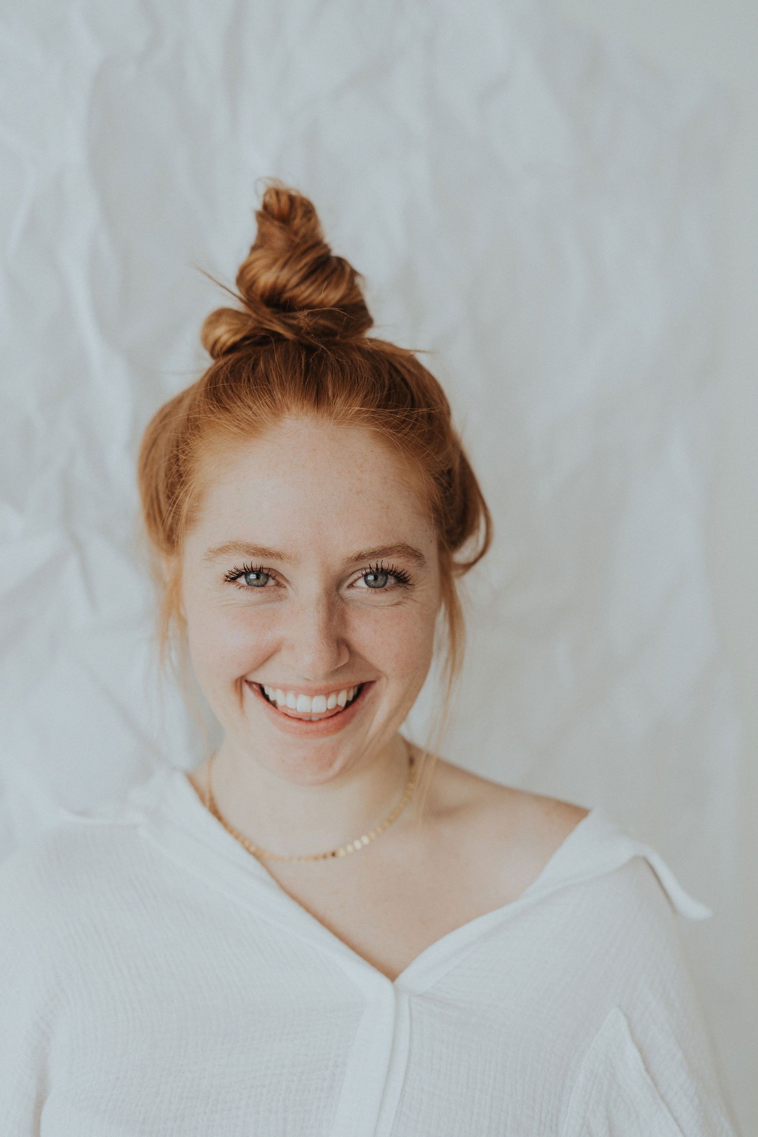 A redhead woman stands against a white wall