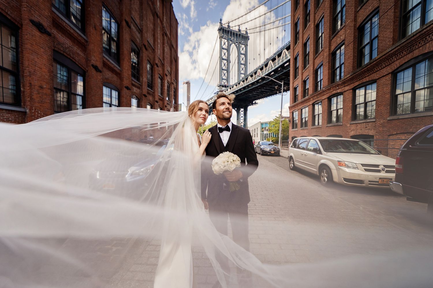 Urban wedding photo with flowing veil against Manhattan Bridge backdrop in DUMBO Brooklyn.