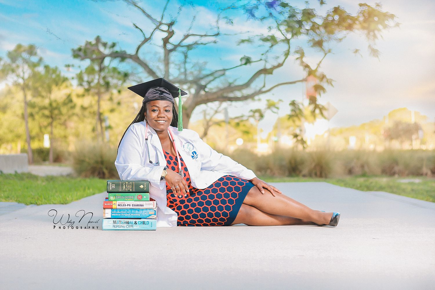 Female graduate in white coat and cap sits outdoors with medical books, celebrating nursing school graduation.