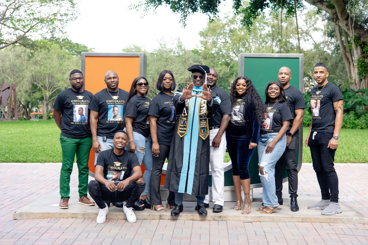 Group of family and friends pose outdoors with graduate wearing cap and gown in front of colorful wall.