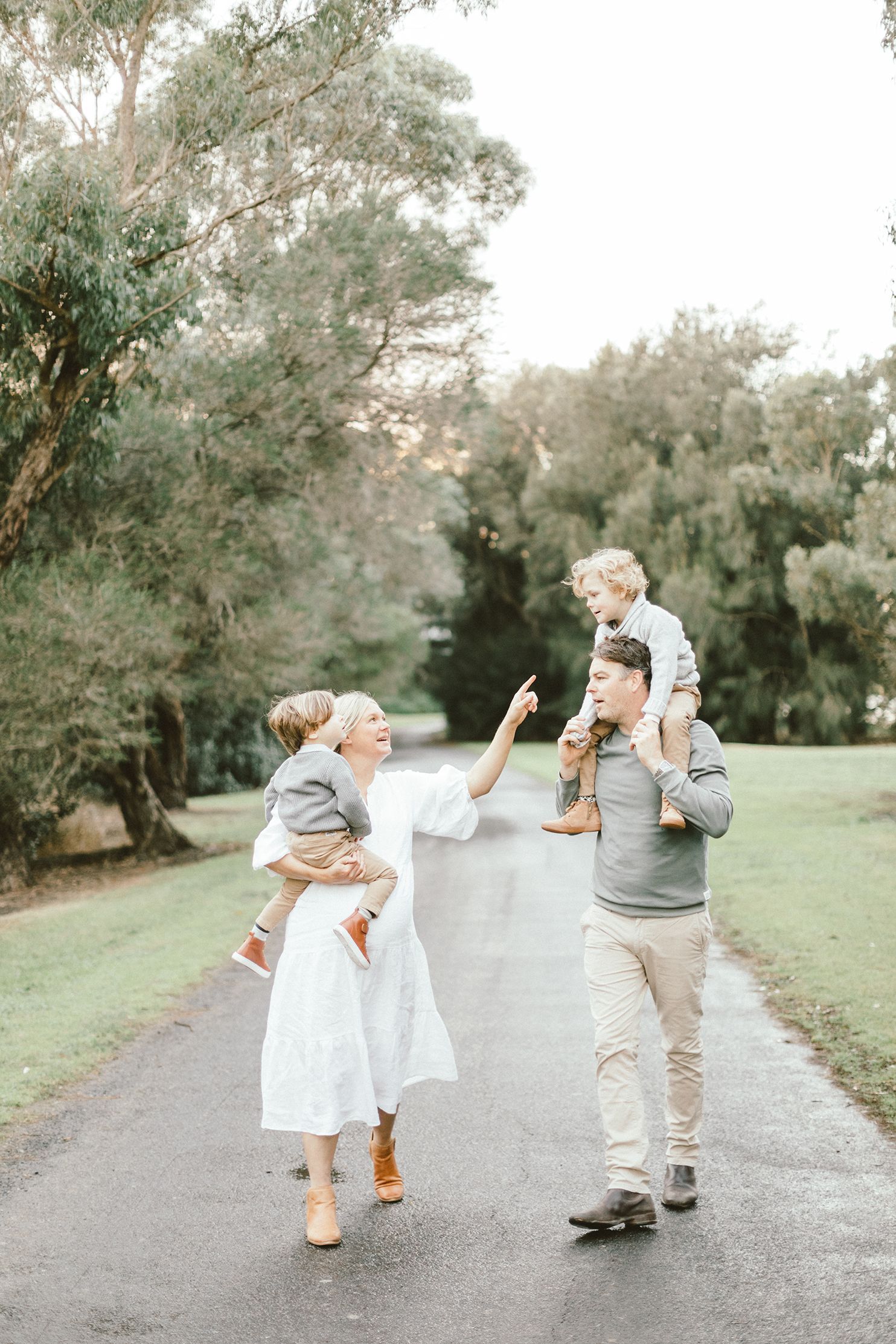A touching outdoor family photoshoot shows playful moments between family members on a tree-lined path.