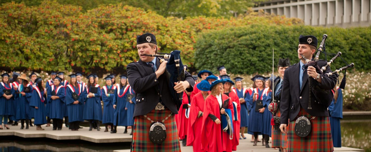 Bagpipers lead graduates during outdoor commencement ceremony.