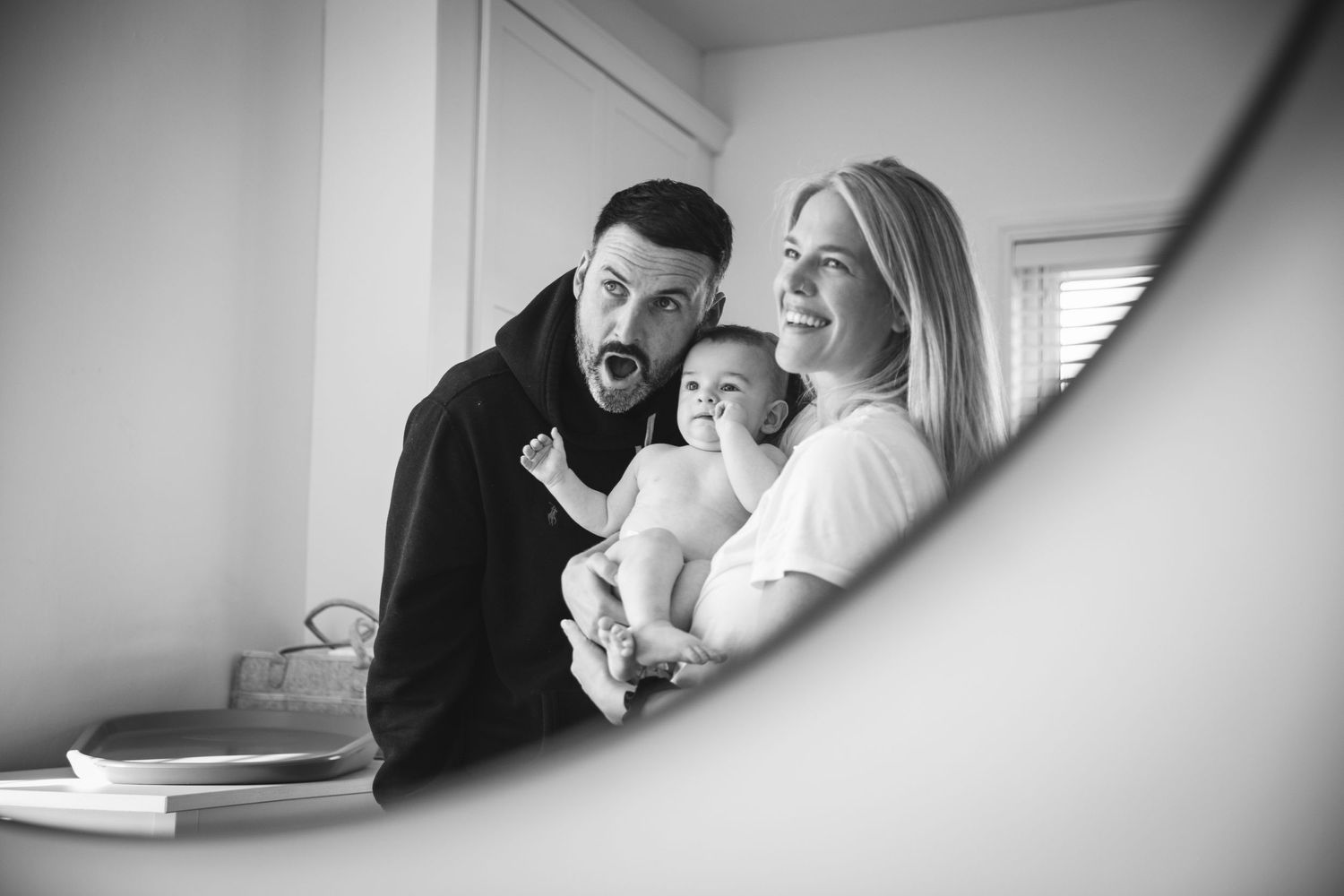 Black and white mirror image shows joyful family moment with baby.