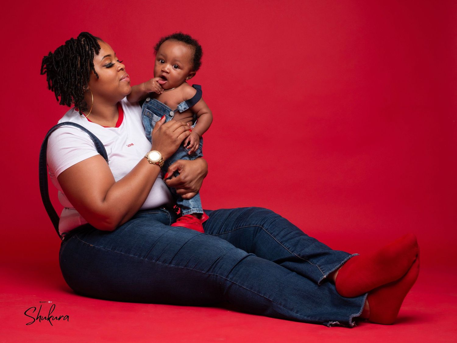 Parent playing with baby while sitting on floor against vibrant red background.