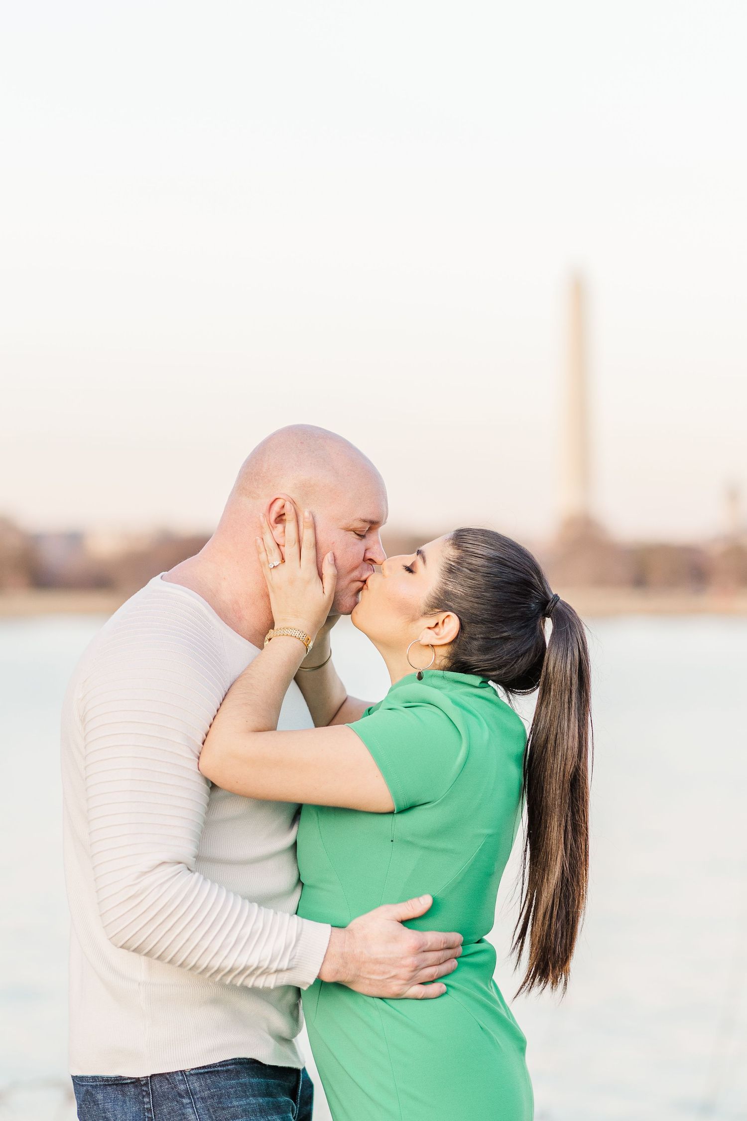 Romantic embrace captured during sunset with water and monument in background.