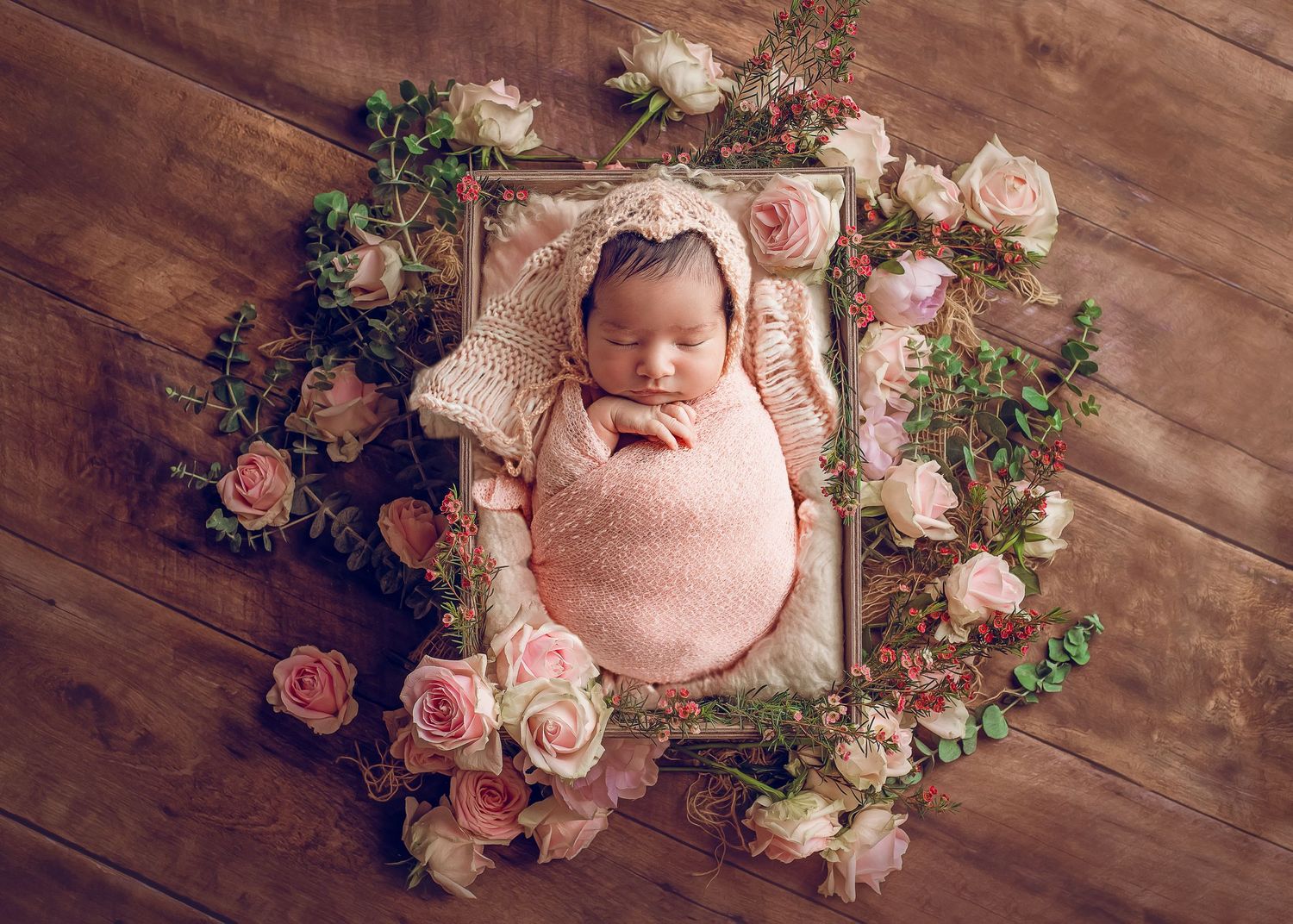 newborn baby wrapped in pink in crate surrounded by flowers vintage look