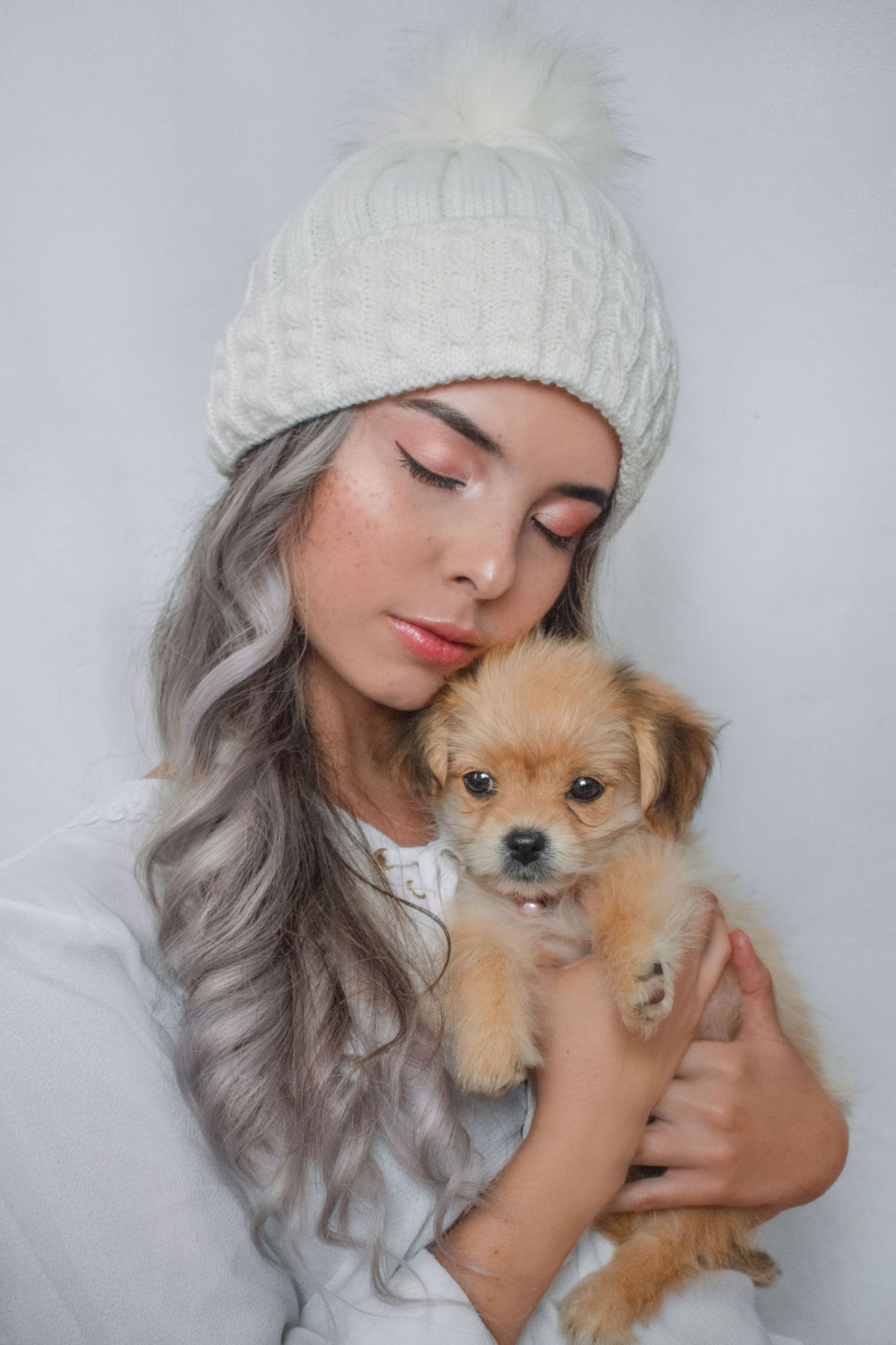 Cozy winter portrait featuring silver hair, white knit beanie, and small puppy.