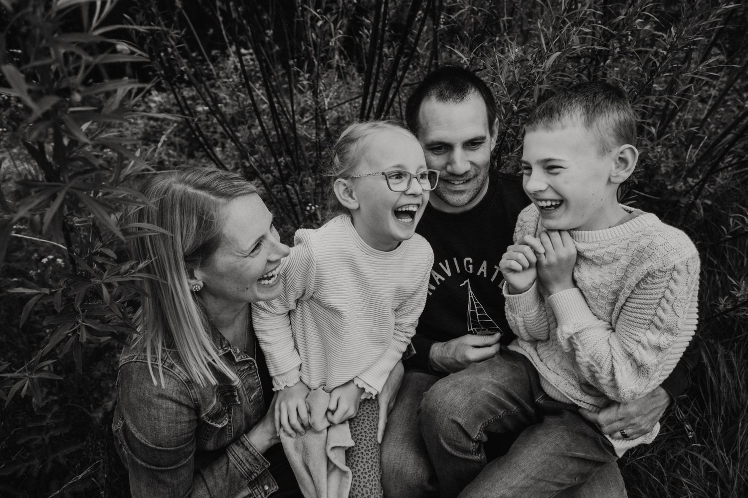 Black and white family portrait showing joyful laughter in garden setting.