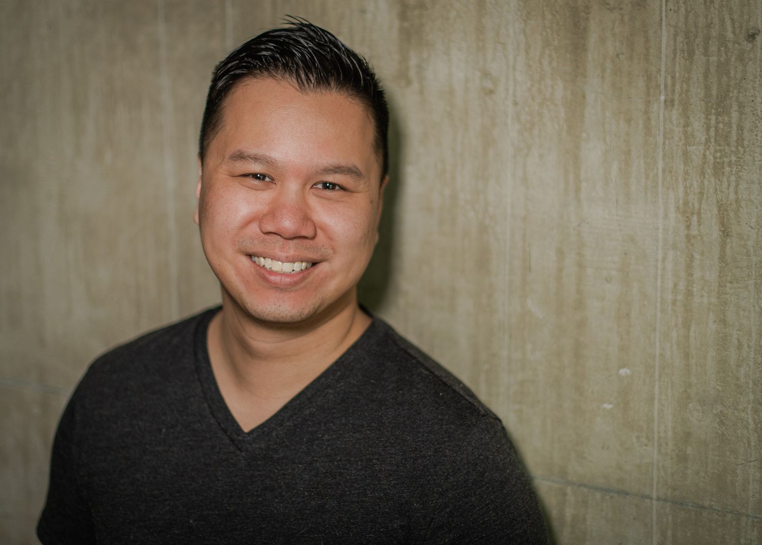 a smiling young Vietnamese man leans against a wall