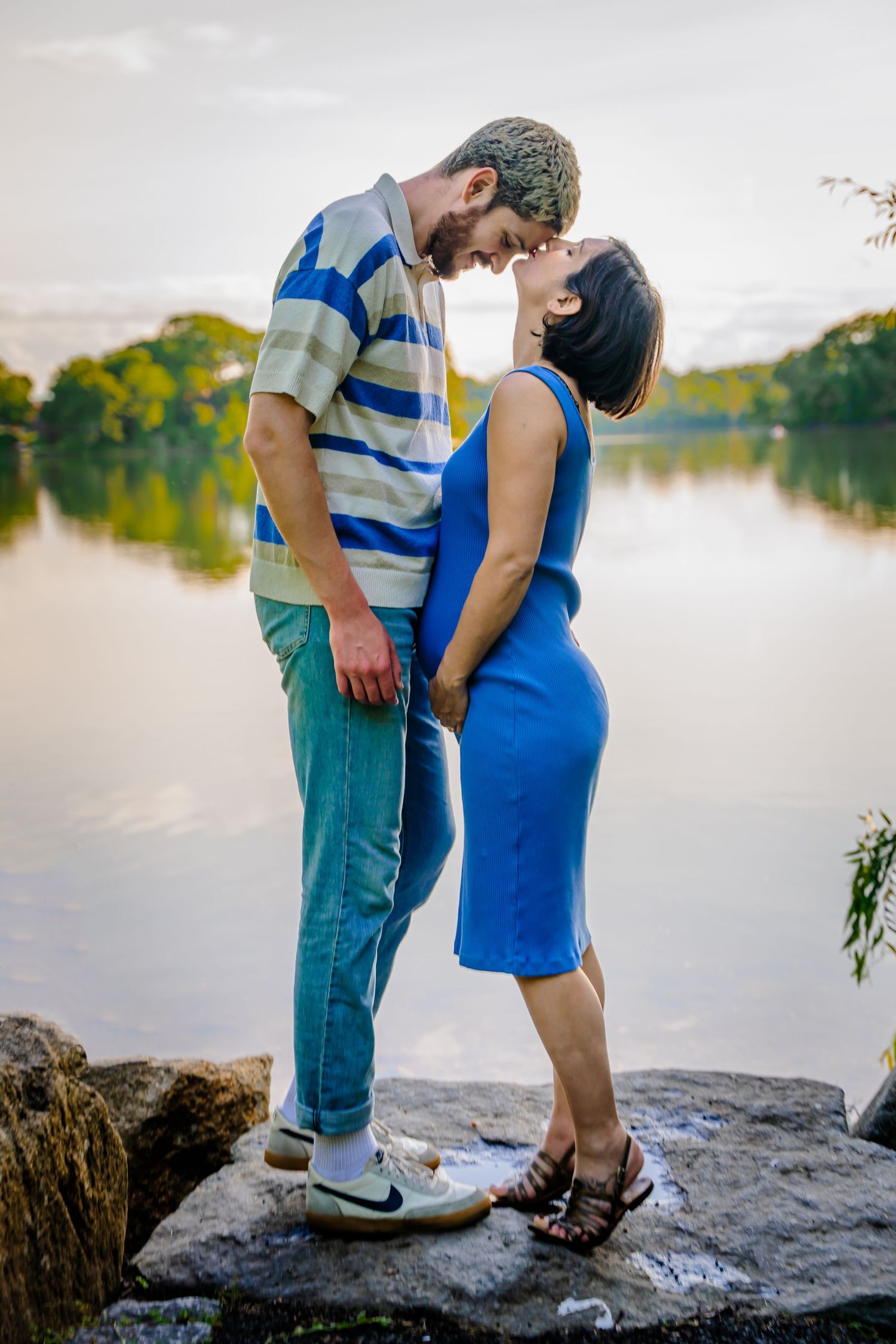 Romantic couple embracing on rocks by a serene lake at sunset.