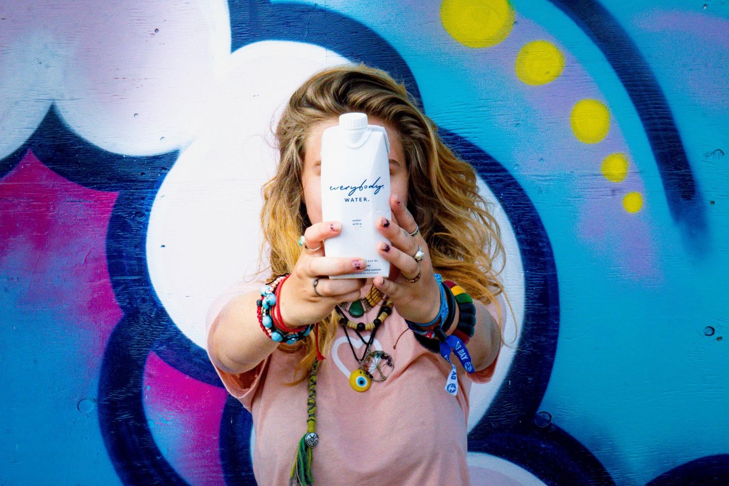 Person holds white coffee cup against vibrant street art mural background.