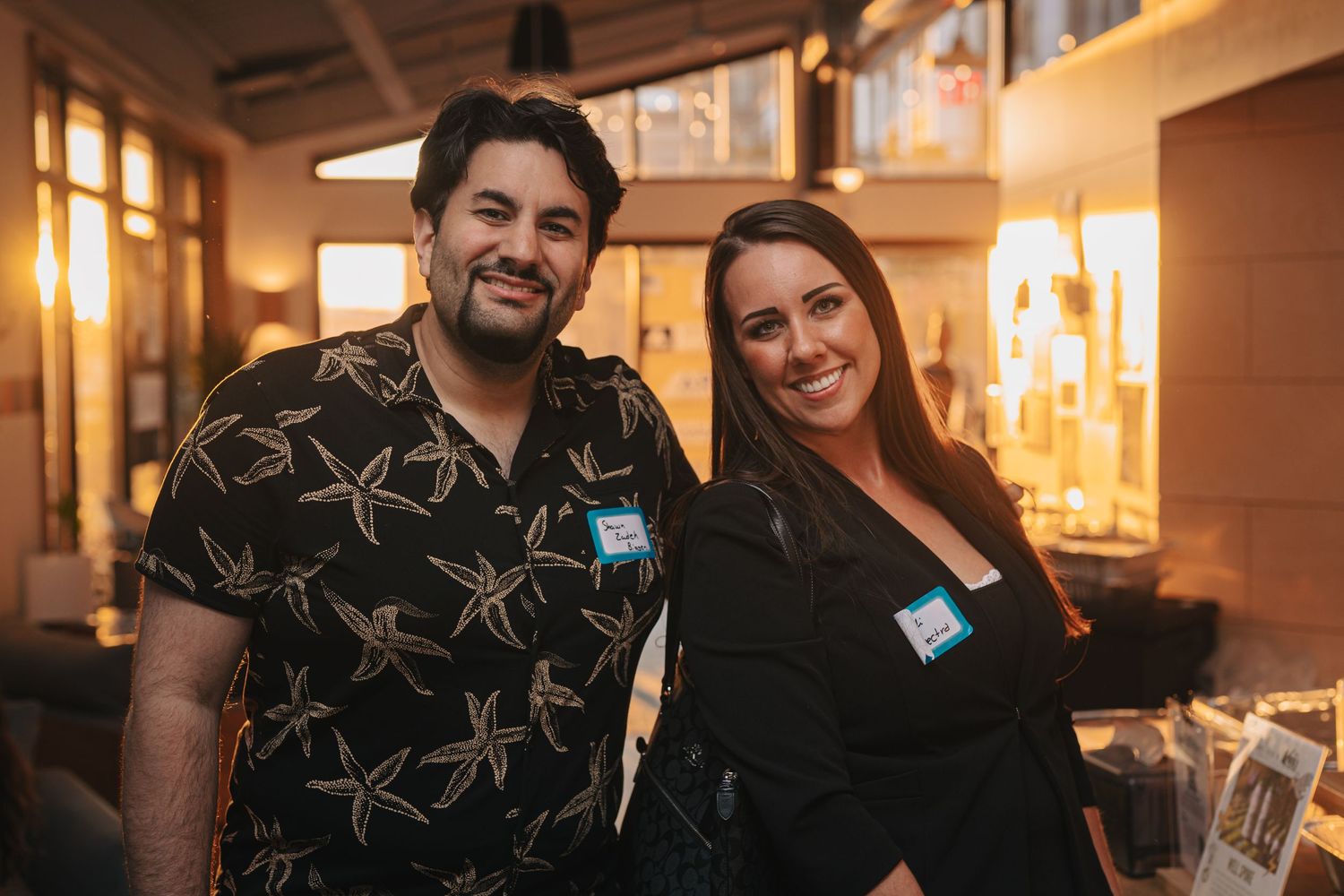 Two colleagues wearing name tags pose together at networking event.