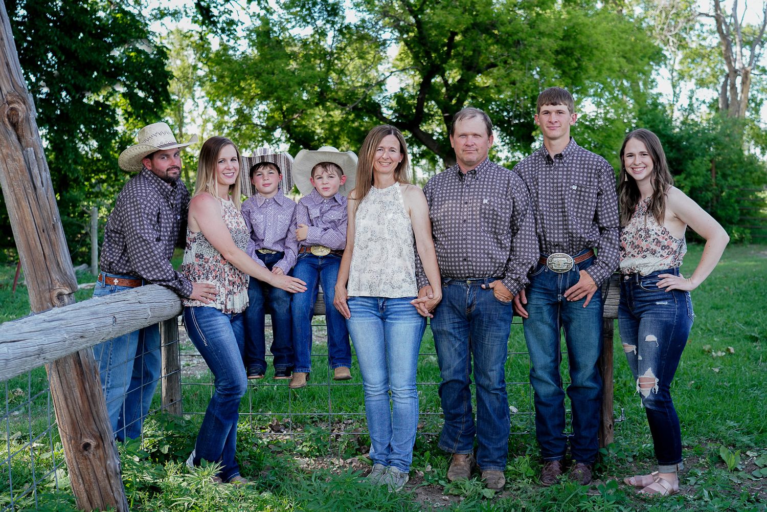Large family group portrait session outdoors by wooden fence in casual western attire.