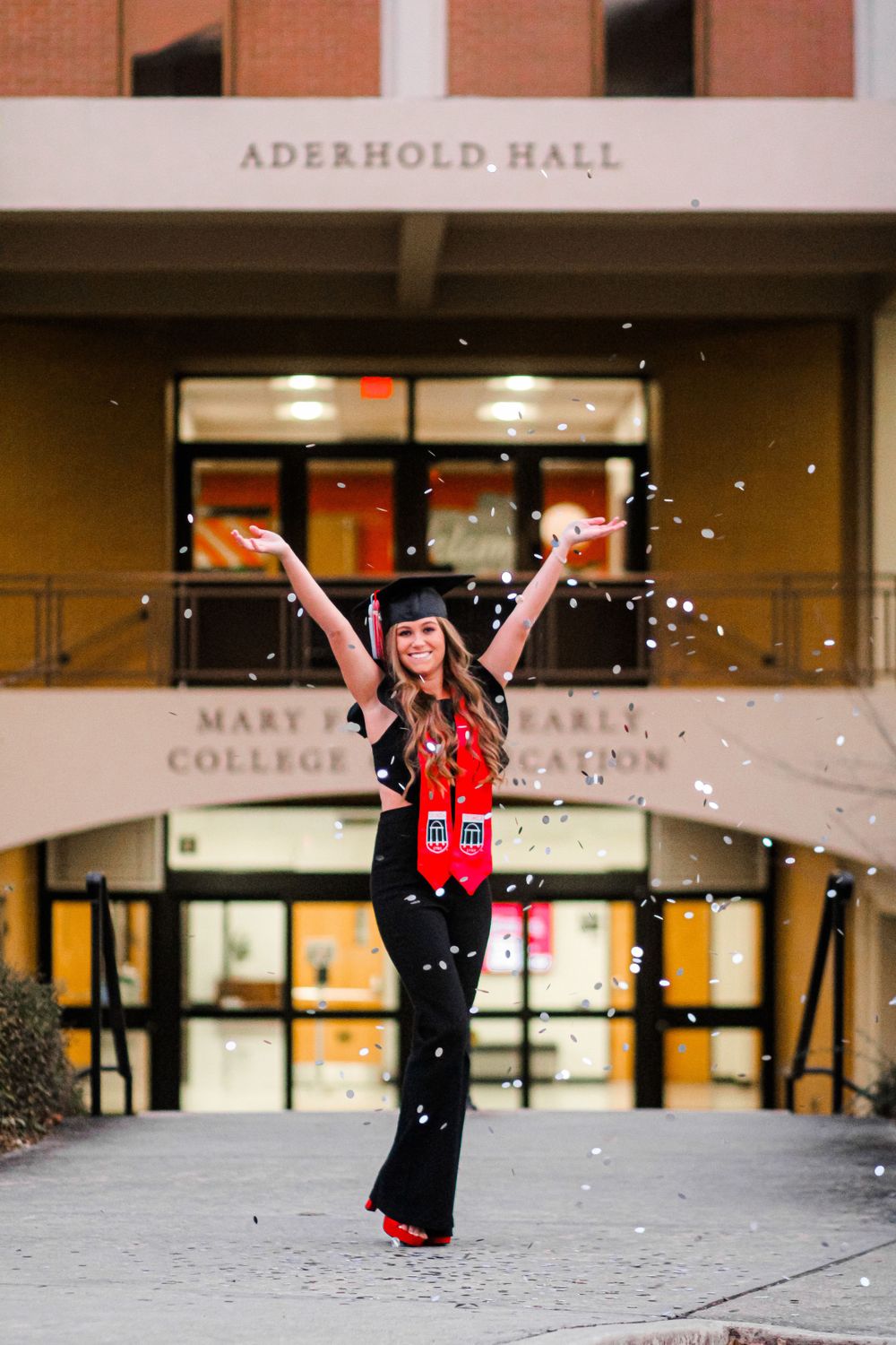 Graduate celebrating with confetti outside Aderhold Hall building.