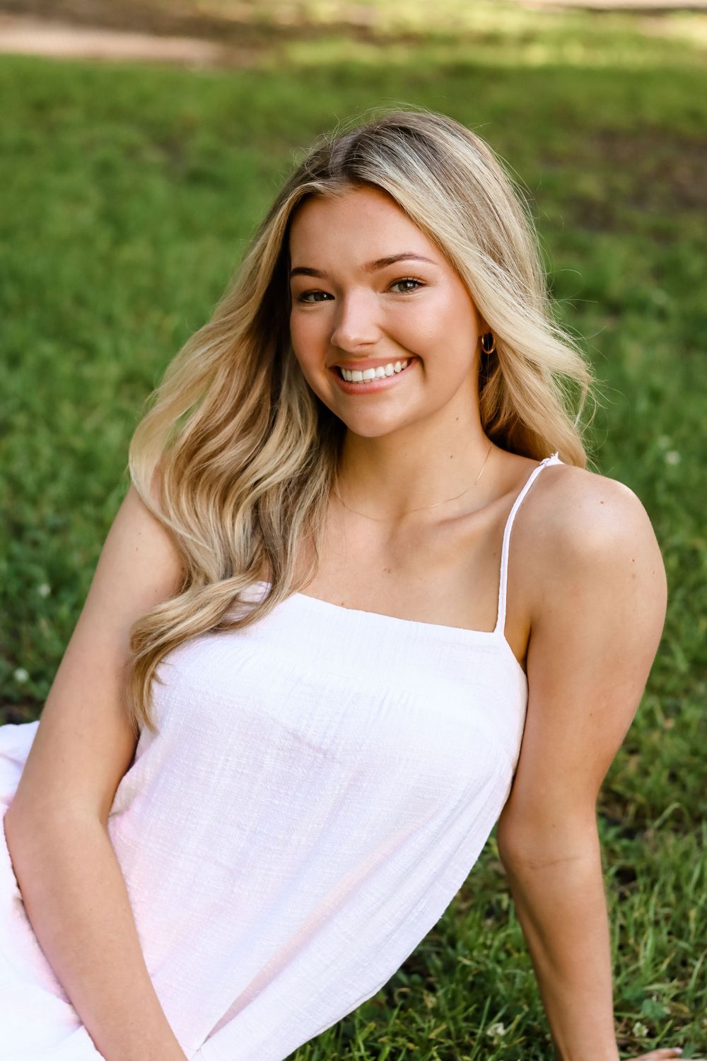 Portrait of woman in white top outdoors on sunny grass lawn.