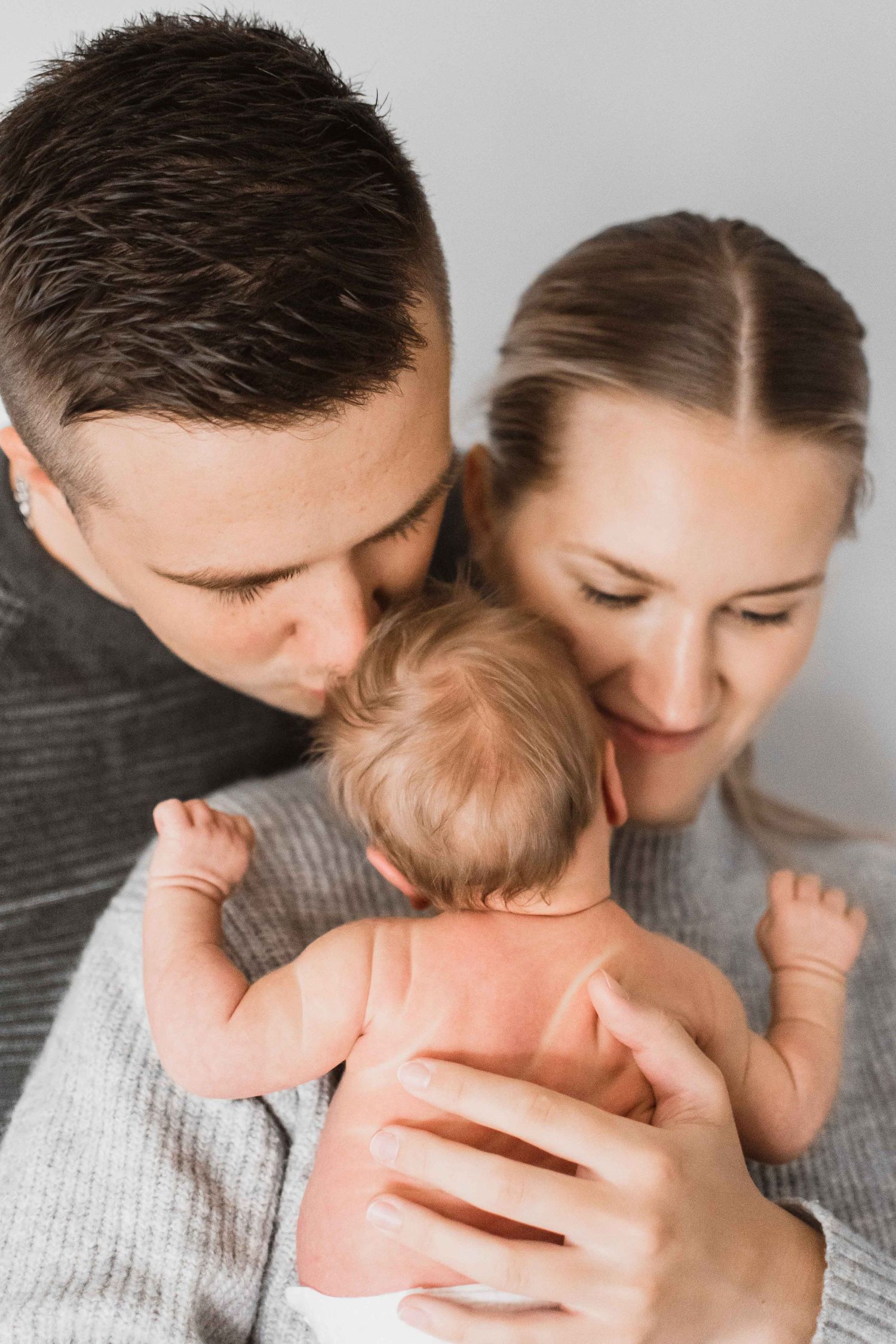 Intimate family portrait showing parents sharing tender moment with their infant.