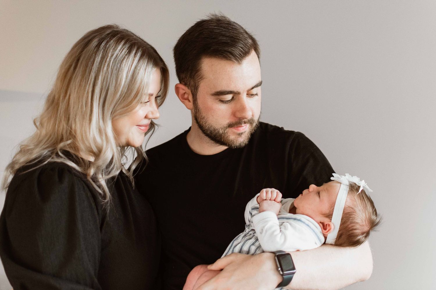 Parents in black clothing holding newborn baby in white outfit.