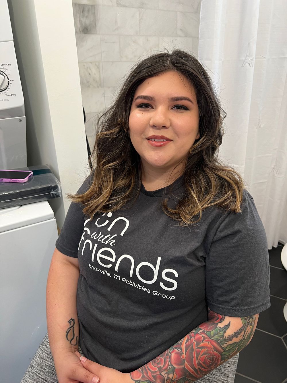 Person in black Friends t-shirt with visible arm tattoos sitting by window.