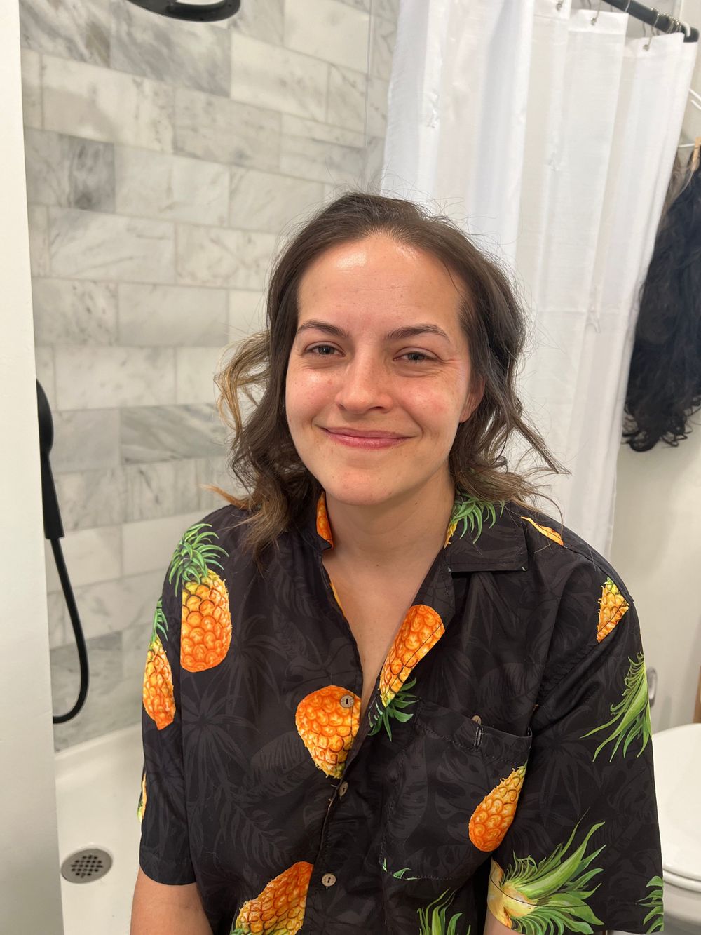 Person wearing black shirt with pineapple print sitting in front of white curtains.