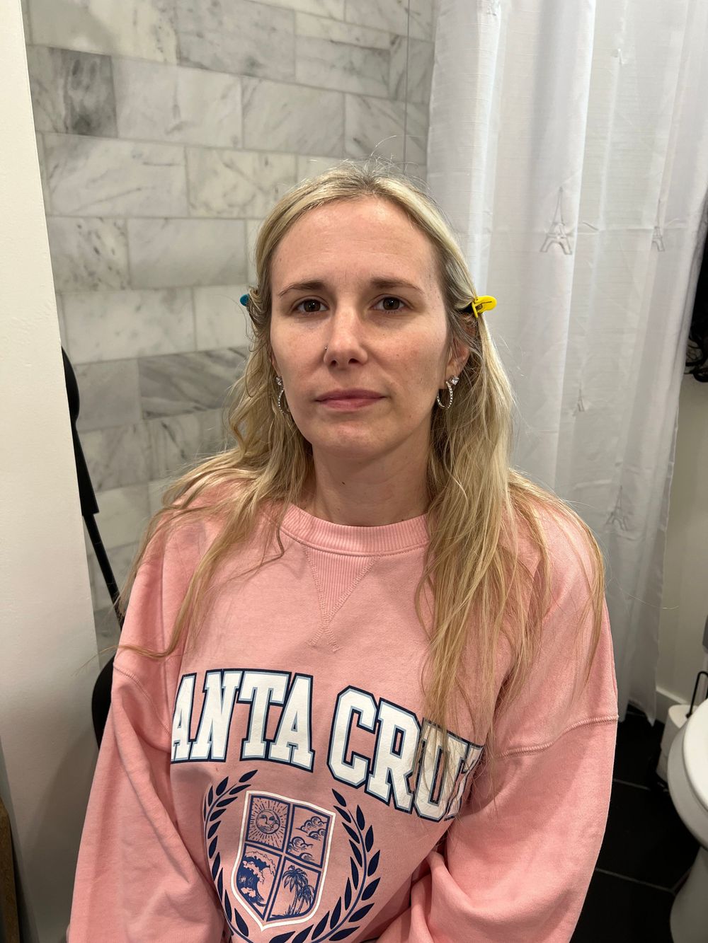 Person wearing a pink collegiate sweatshirt sitting against white and grey background.