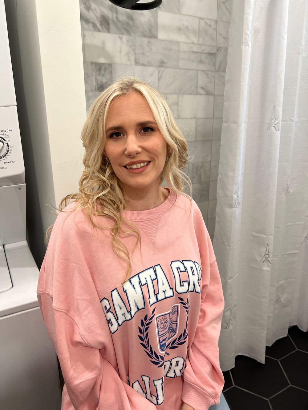 Person in pink collegiate sweatshirt with navy logo smiling at camera.