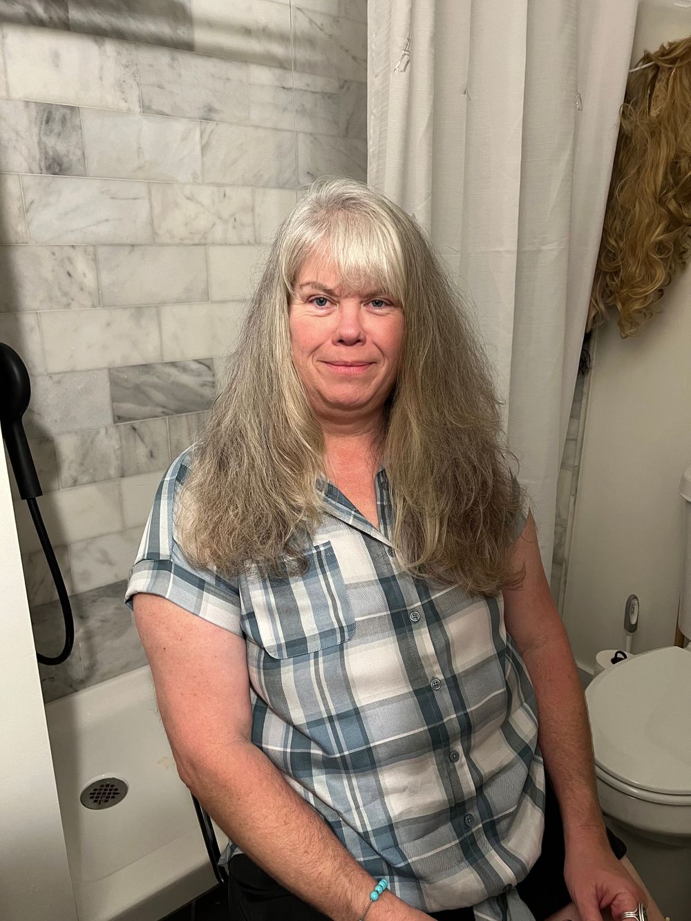 Person in plaid shirt sits in bathroom with textured marble walls.