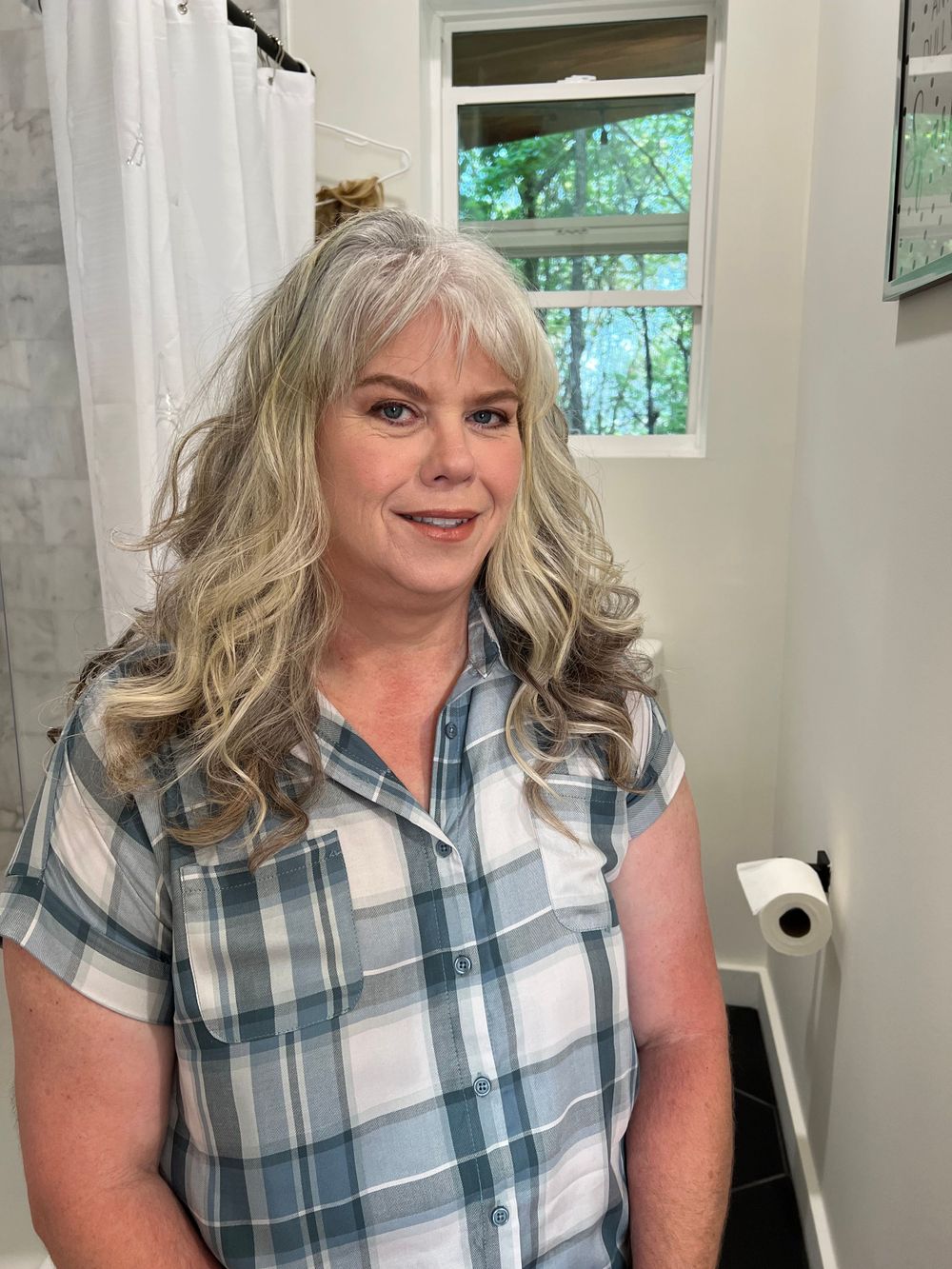 Person in blue and white plaid shirt poses in bathroom interior.