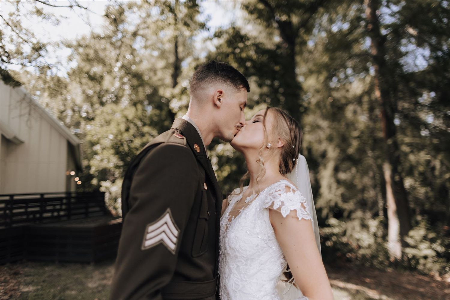 Intimate outdoor moment between military member and bride near rustic building.