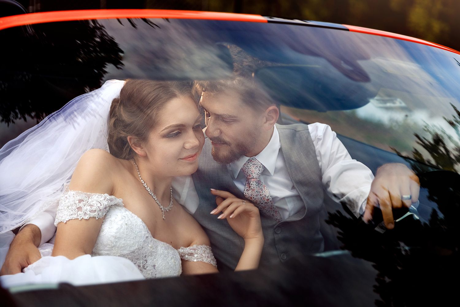 A romantic wedding photo through a car windshield with reflections and natural light.